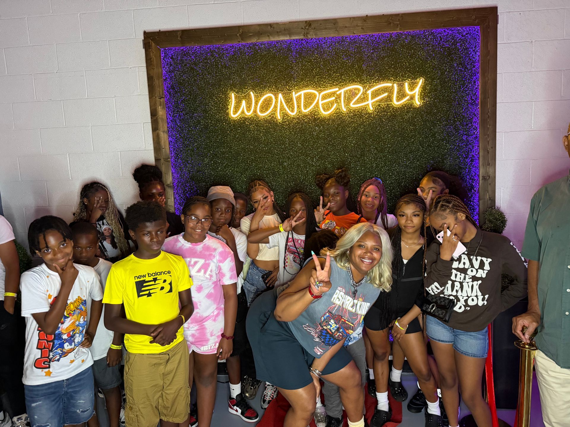Group posing in front of a glowing “WONDERFUL” wall sign, with several making peace signs.