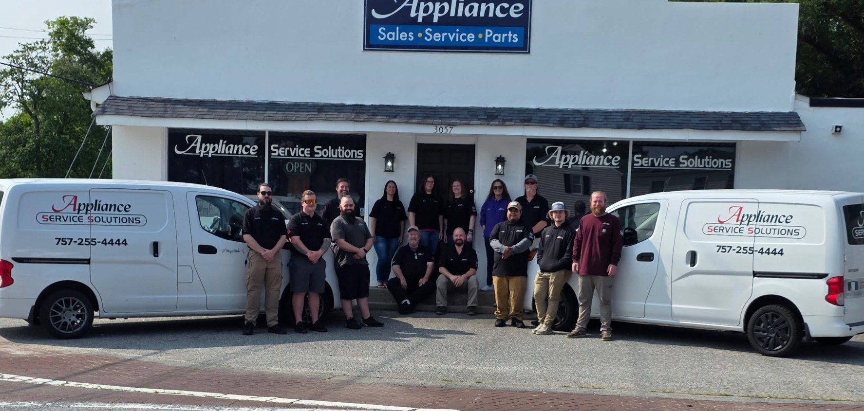 A group of people standing in front of a white building with two white vans parked on the left and right.