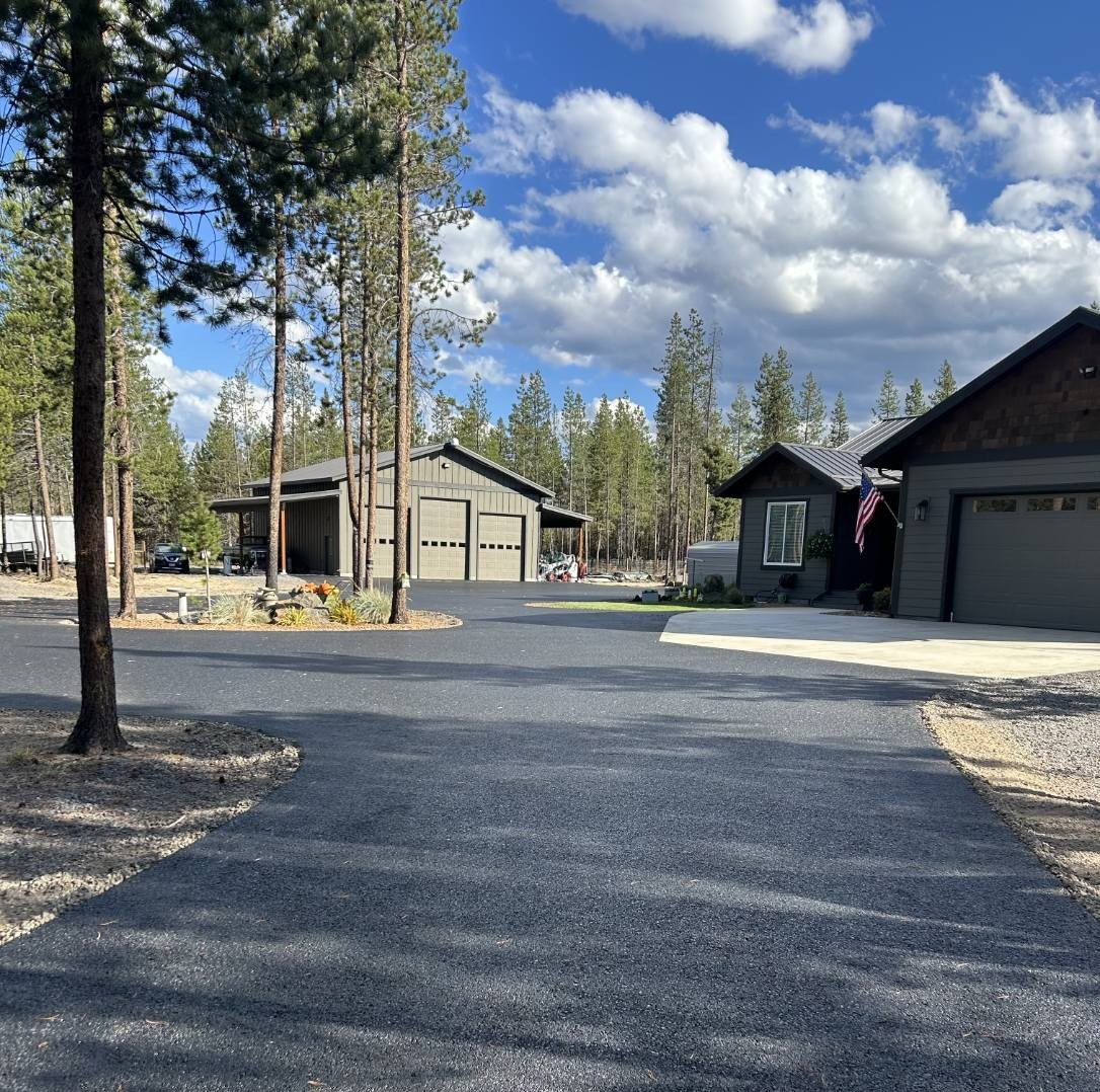 Gravel driveway between cabins and pine trees under a partly cloudy blue sky