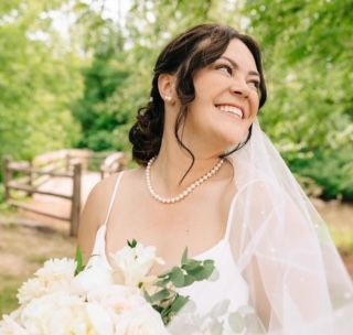 A bride in a white dress and veil is holding a bouquet of flowers and smiling.