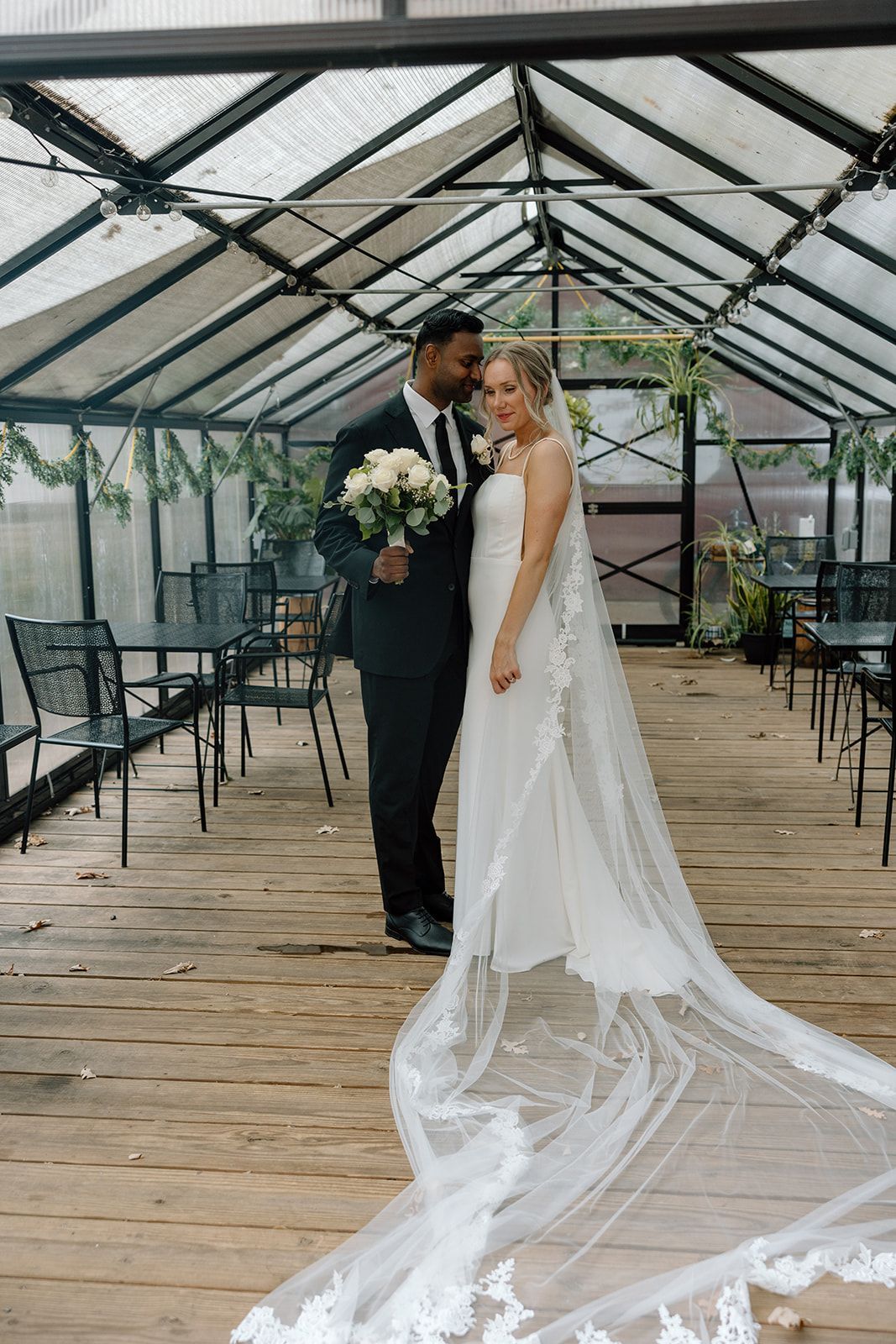 A bride and groom are posing for a picture in a greenhouse.
