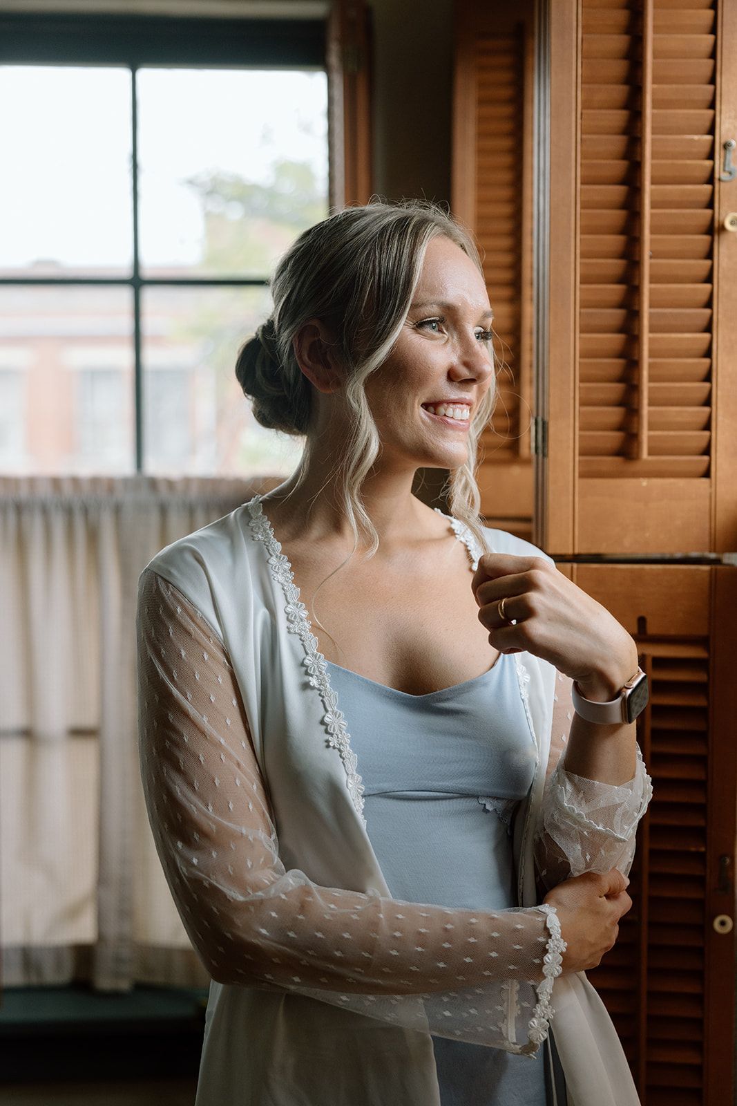 A woman in a white robe is standing in front of a window.