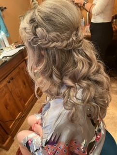 A woman is sitting in a chair with her hair in a half up half down braid.