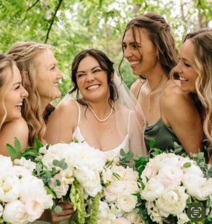 A group of women are standing around a bride holding a bouquet of flowers.