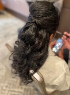 A woman is sitting in a chair with her hair in a half up half down ponytail.