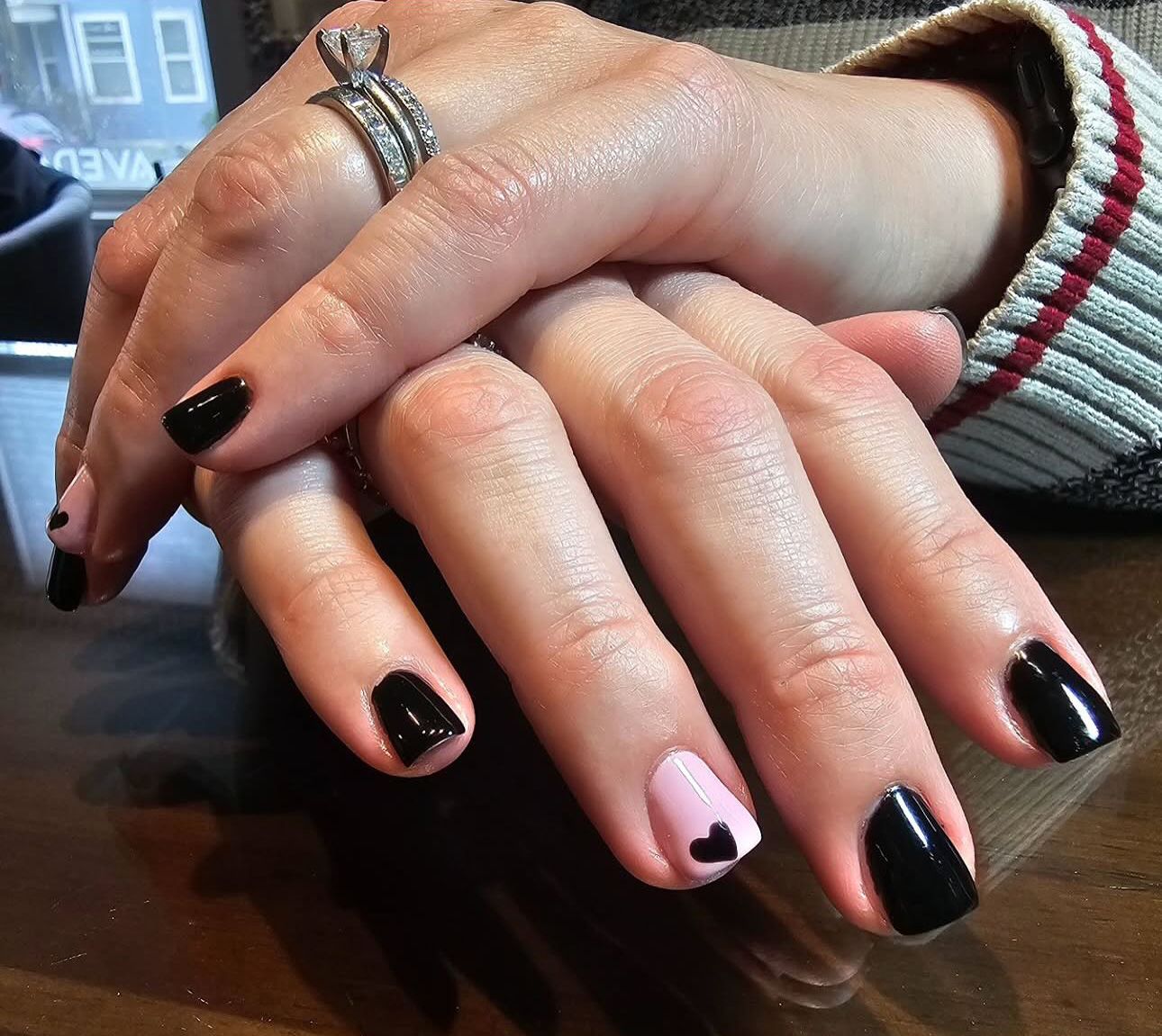 A woman 's hands with black and pink nails and a ring on her finger