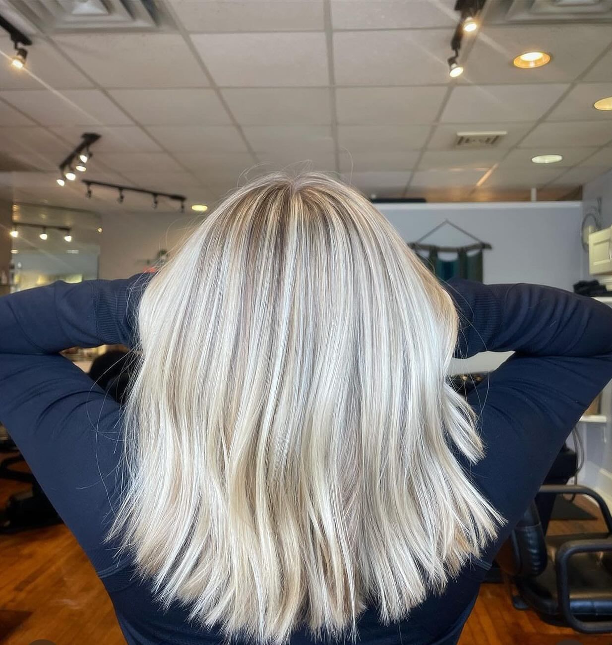 A woman with blonde hair is standing with her hands behind her head