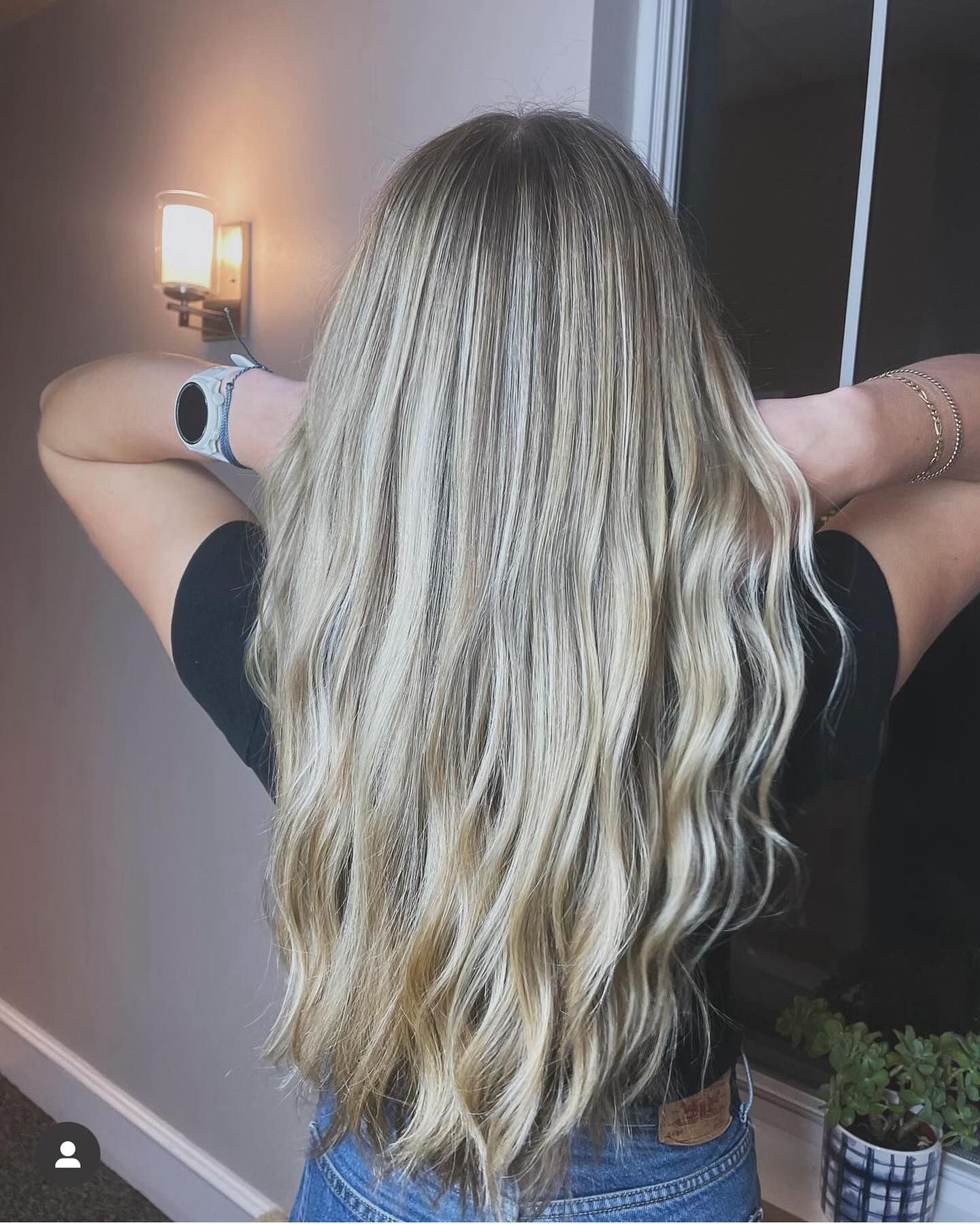 A woman with long blonde hair is standing in front of a window.