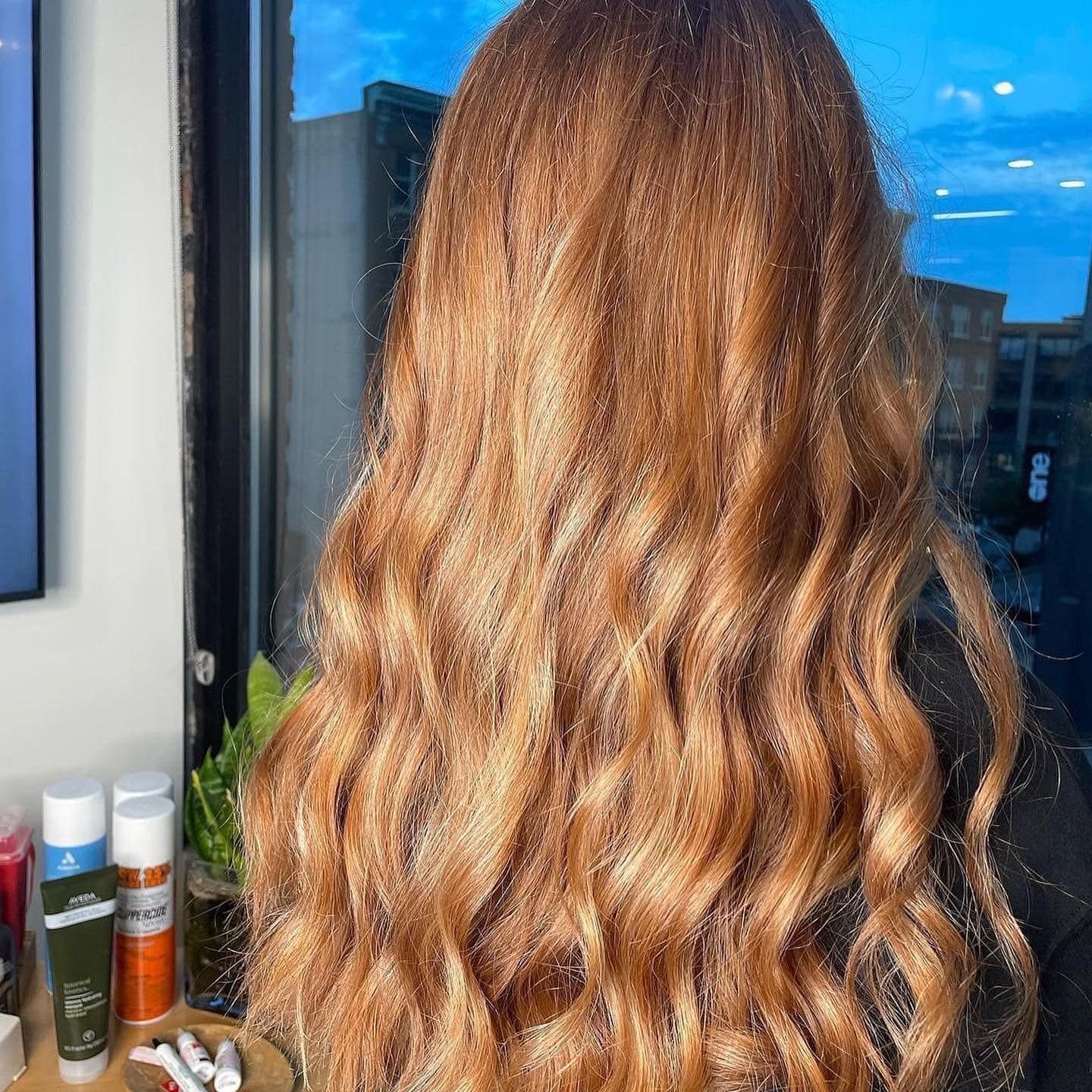 A woman with long red hair is standing in front of a window.