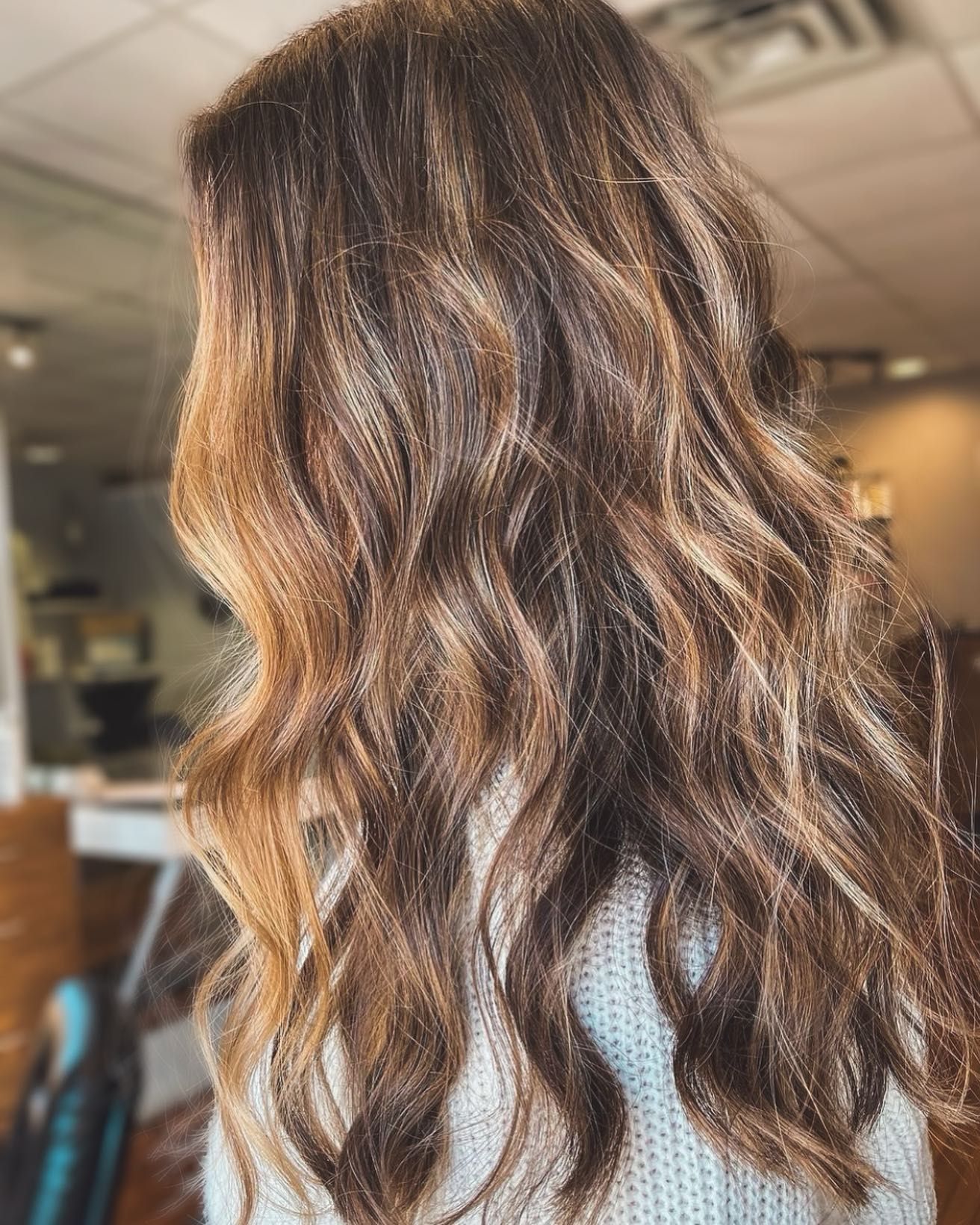 A woman with long wavy brown hair is wearing a grey sweater.