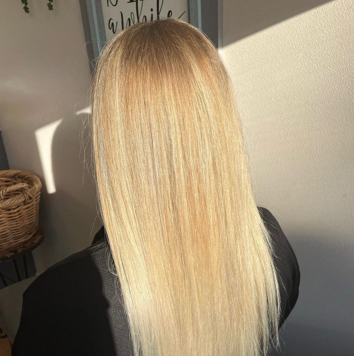 A woman with long blonde hair is sitting in front of a wall.