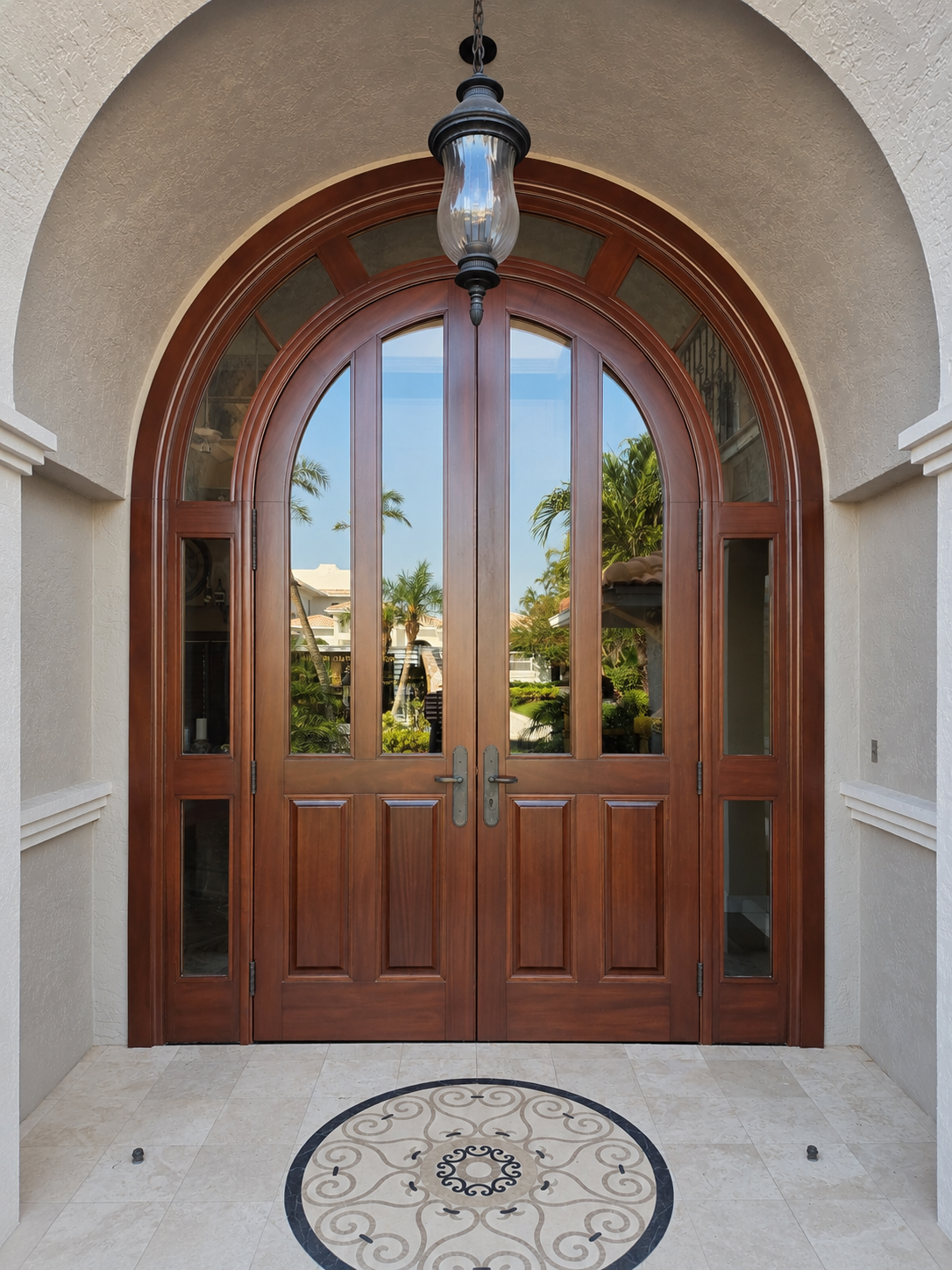 Arched wooden front door with glass panels, framed by stucco walls and a hanging lantern