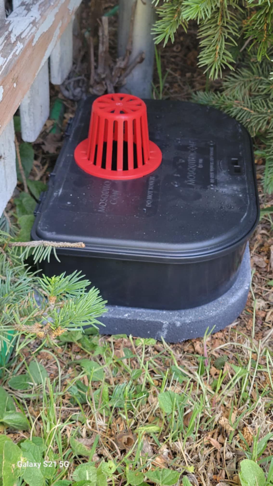 A black box with a red drain on top of it is sitting in the grass