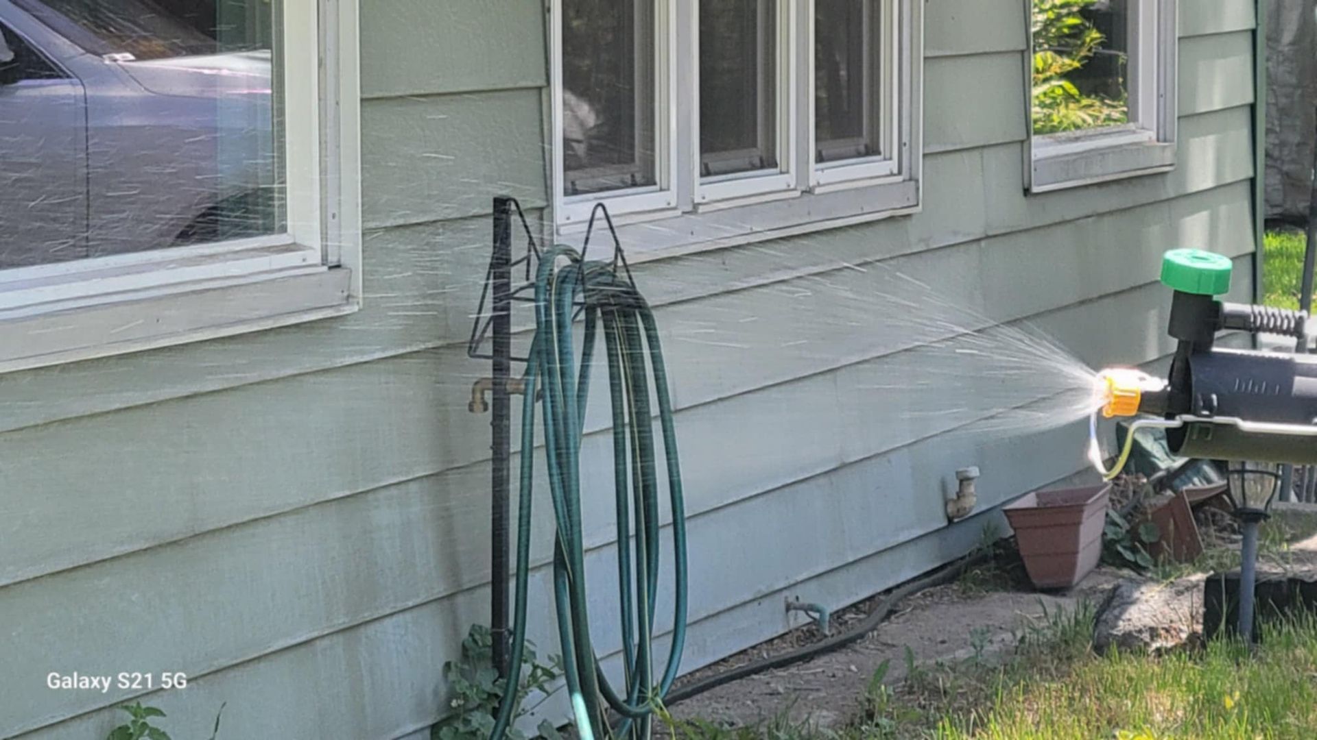 A hose is hanging on the side of a house next to a window