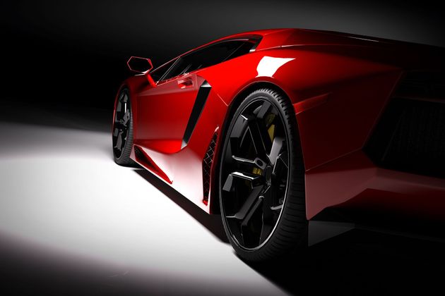 Red sports car, lit from the side, on a white surface against a dark background, showing a wheel.