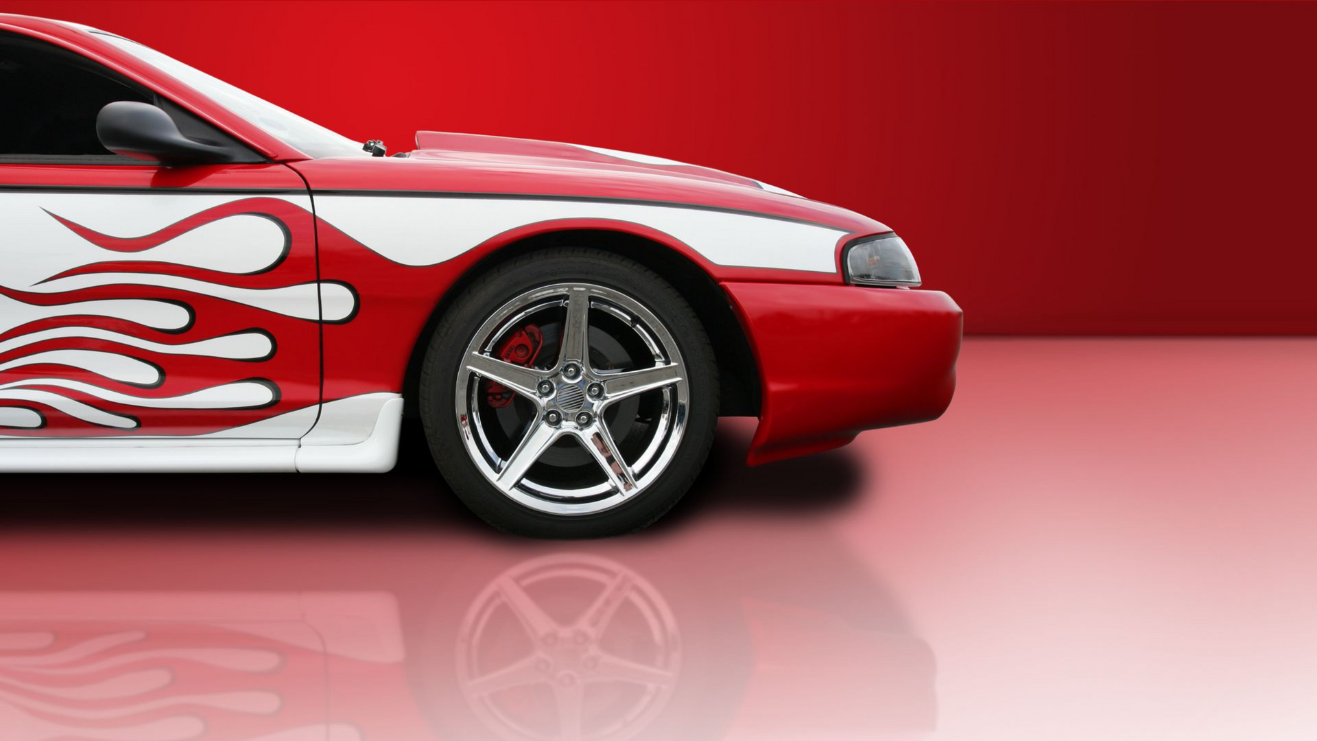 Red sports car with white flame decals, chrome wheels, reflected on a shiny surface.