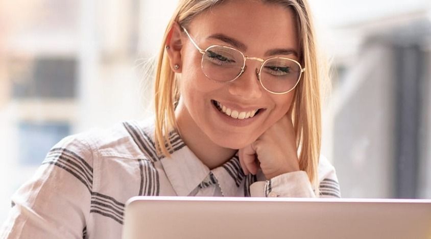 A woman wearing glasses is smiling while using a laptop computer.