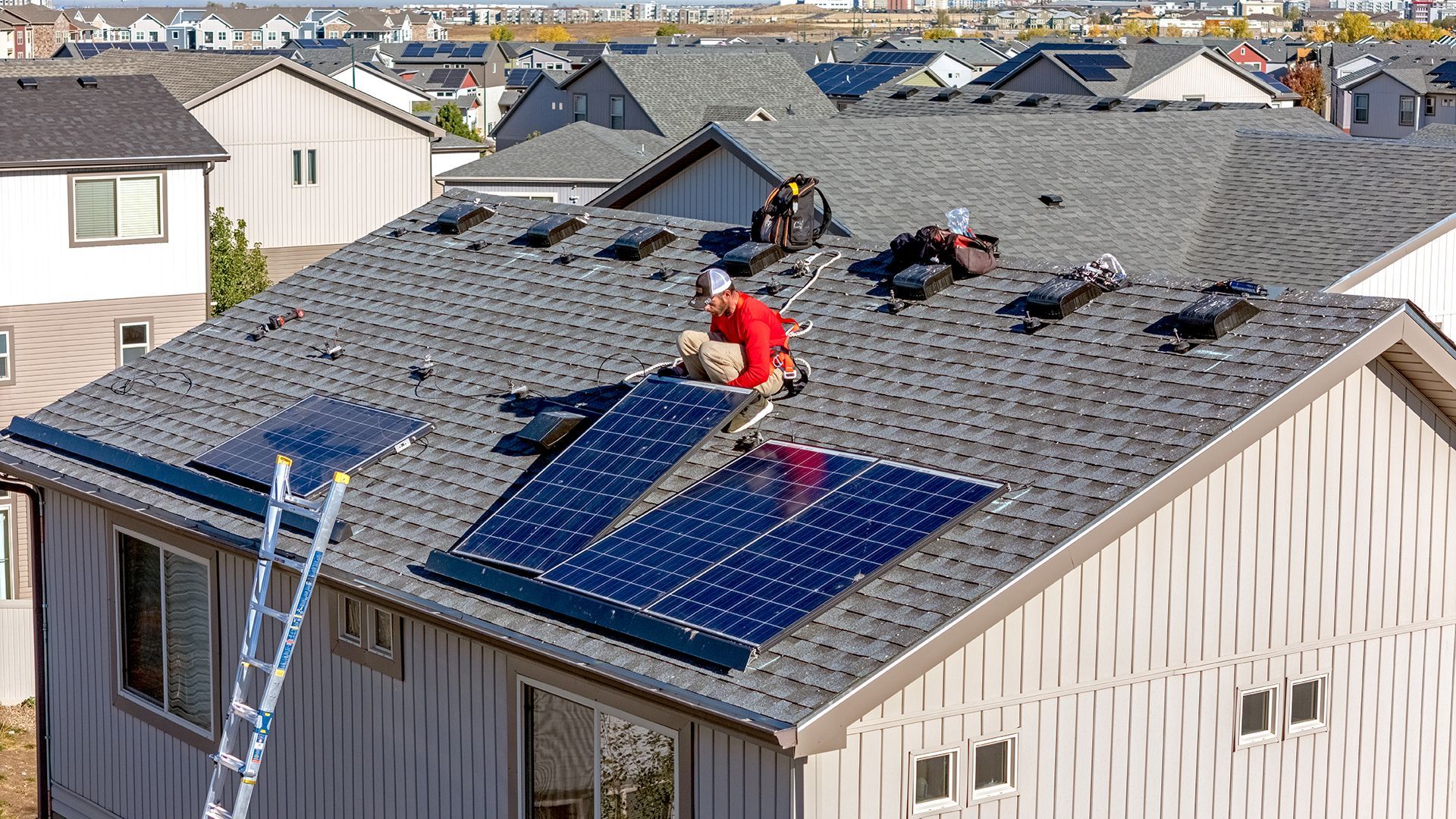 Workers installing solar panels on a residential roof in a sunny neighborhood.