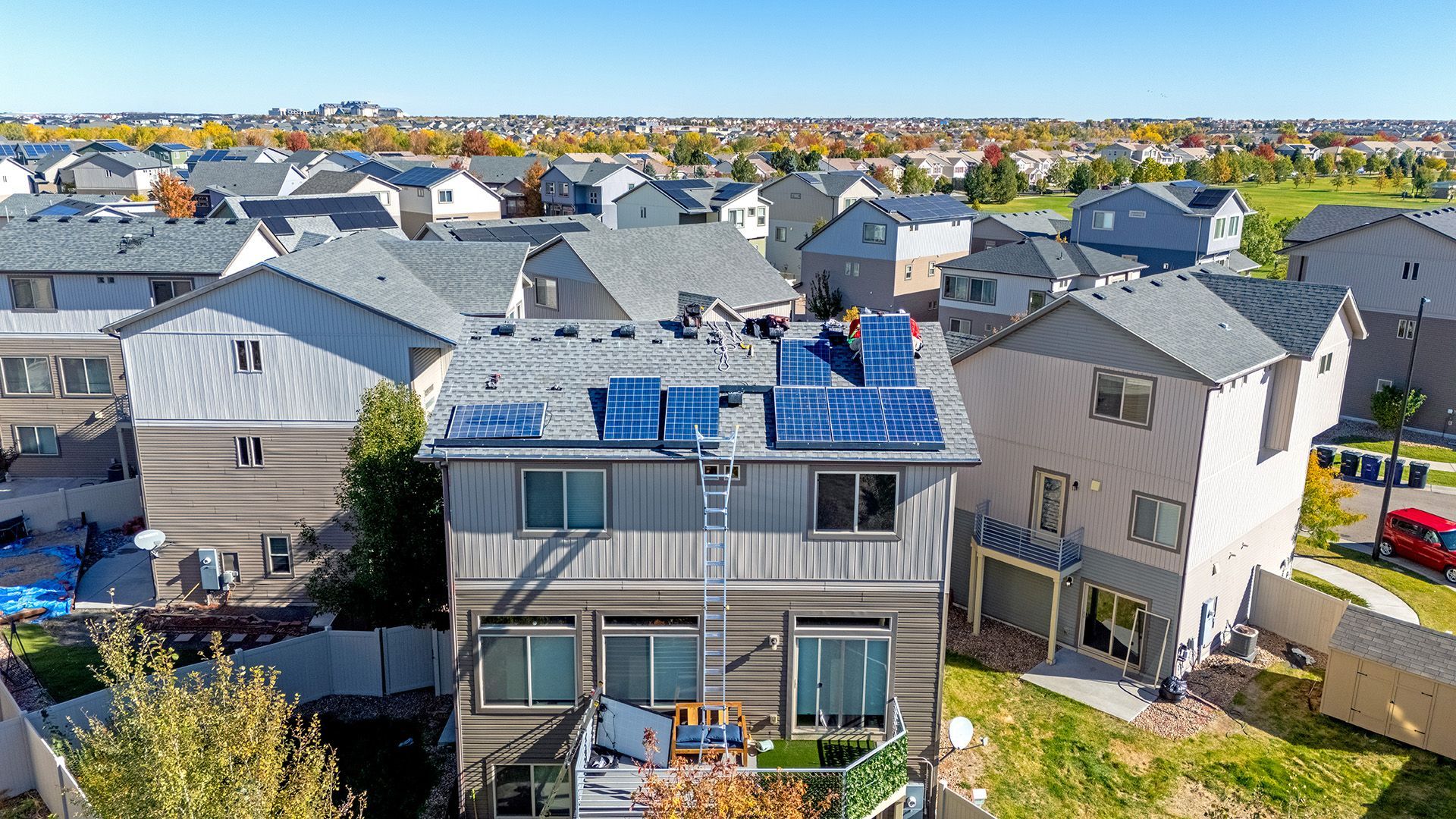 Solar panels on a two-story home's roof in a suburban neighborhood under a blue sky.