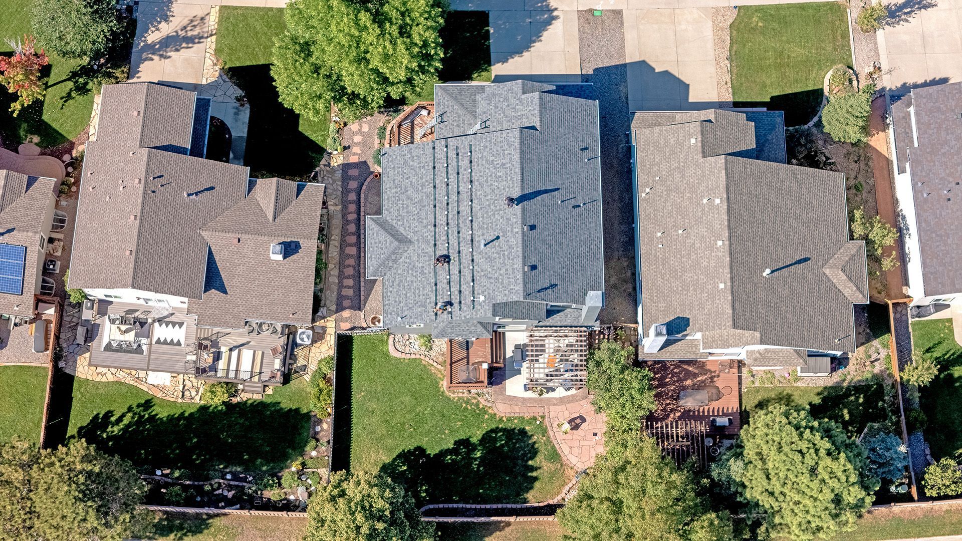 Aerial view of three houses with different roof styles, surrounded by green lawns and trees.