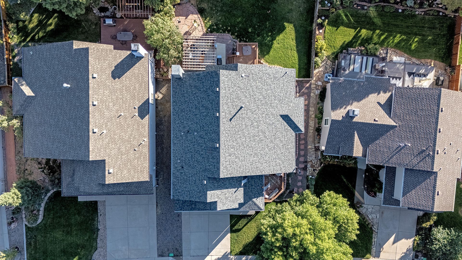 Aerial view of three houses with driveways, yards, and different roof styles.