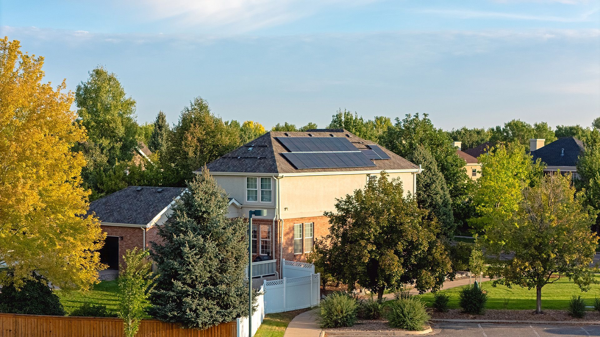 Residential home with solar panels on the roof, surrounded by trees under a blue sky.
