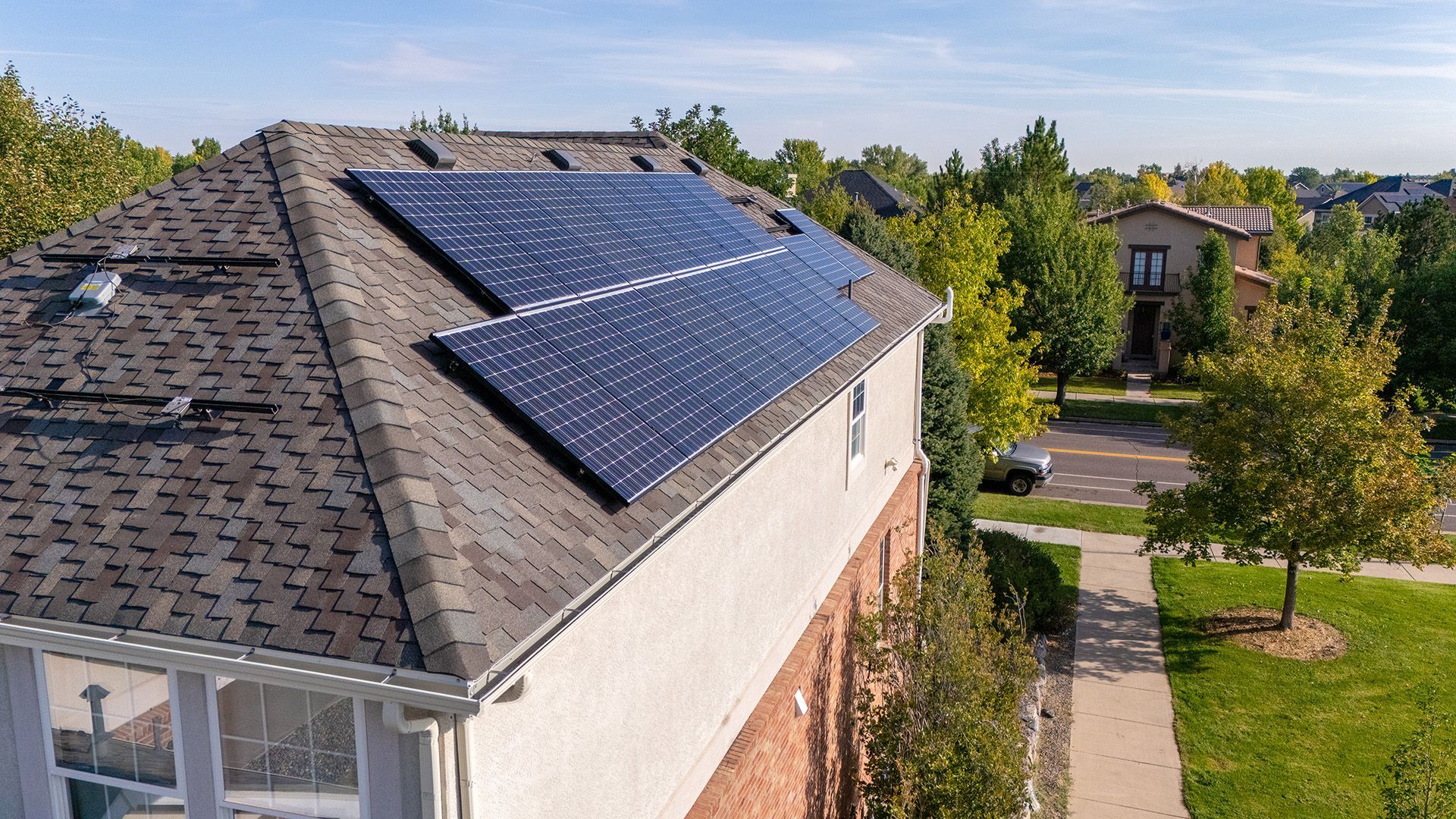 Solar panels on a residential roof, sunny day, surrounded by trees and houses.