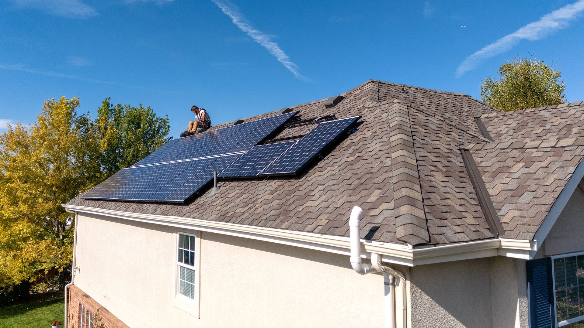 Solar panels being installed on a residential roof; worker on roof, clear sky.