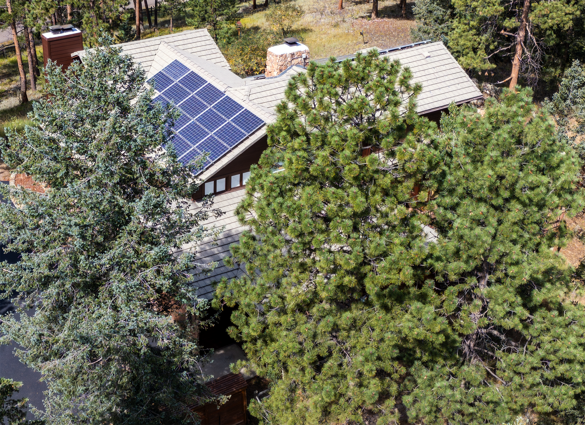 Overhead view of a house with solar panels on the roof surrounded by trees.