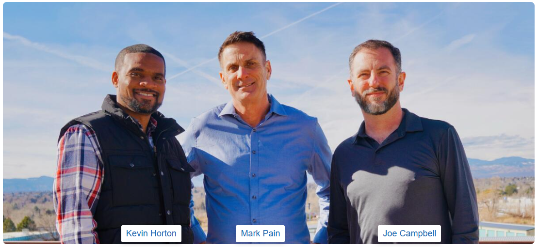 Three men standing outside with a blue sky background; the men are smiling and looking at the camera.