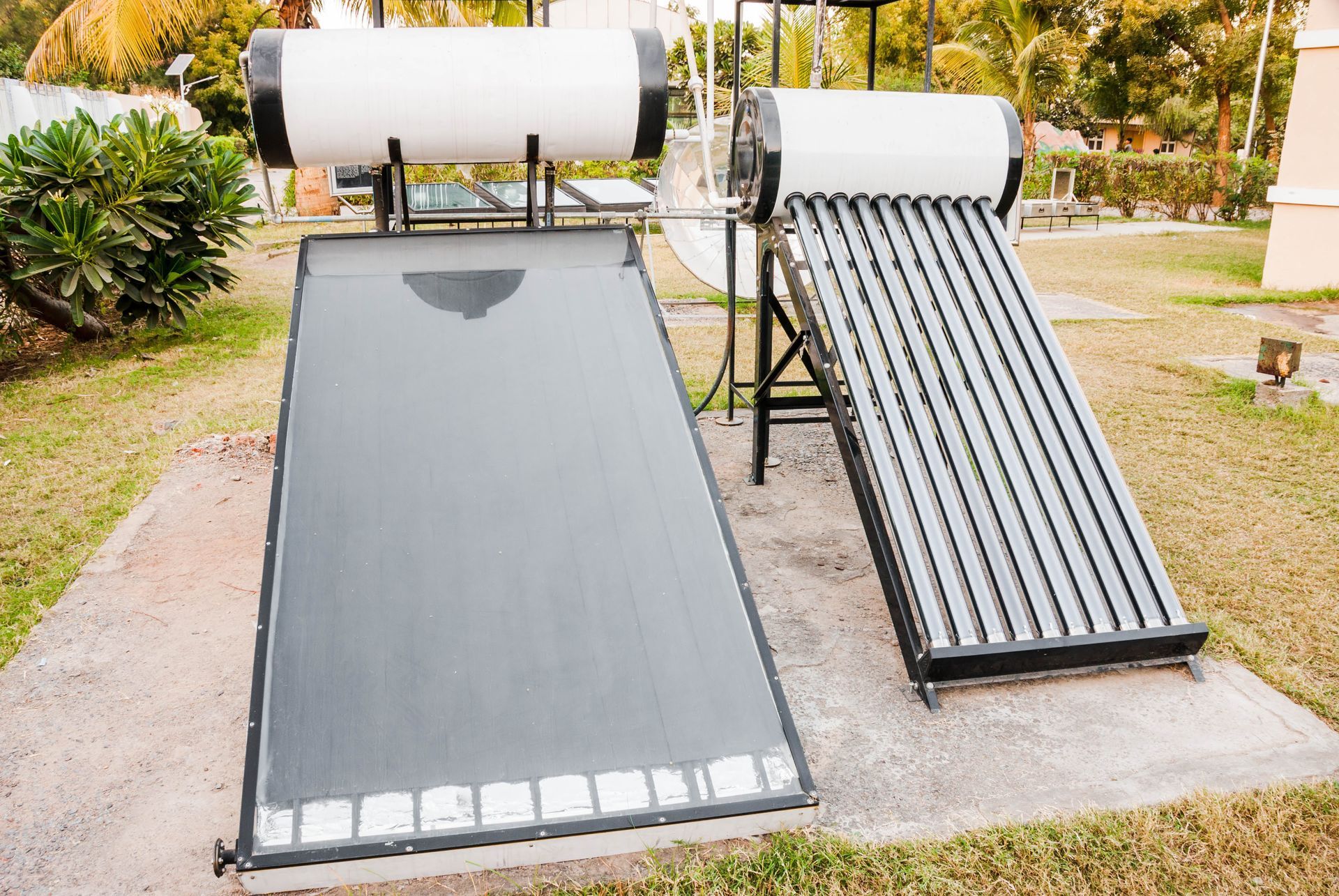 Two solar water heaters on concrete pads in a grassy yard.