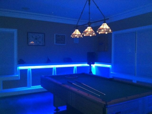Pool table in a room lit with blue LED lights. Three-light fixture hangs above table.