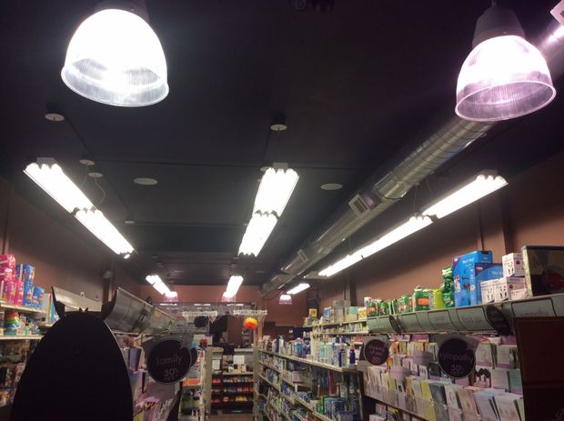 Interior of a store, with bright overhead lights illuminating the shelves of products and the dark ceiling.