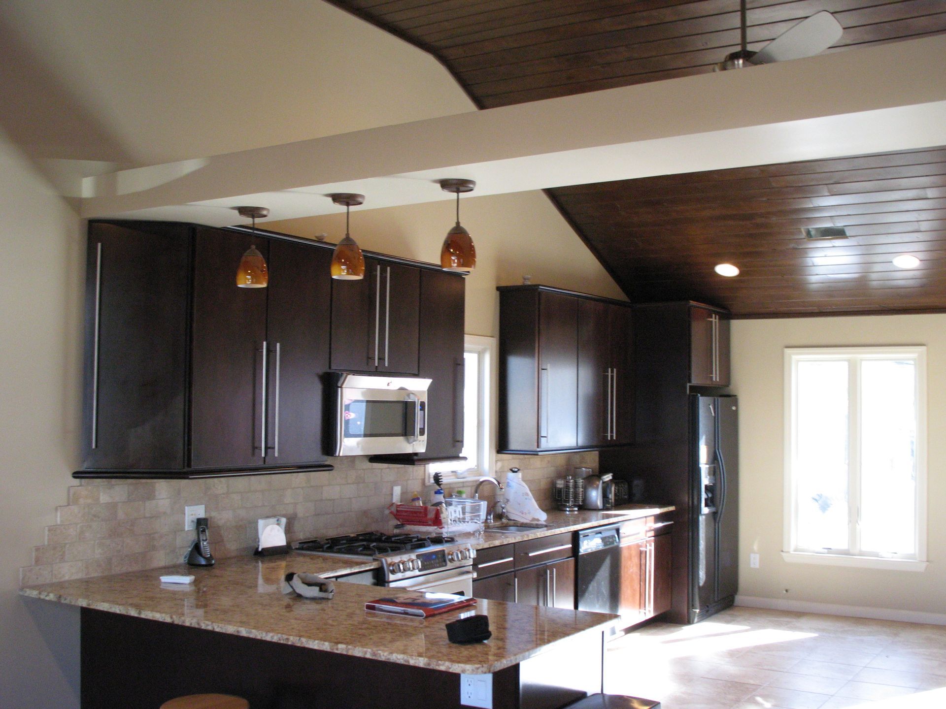 Dark cabinets in a kitchen with a tan countertop, wood ceiling, and pendant lights.