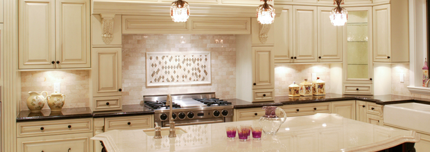 Cream-colored kitchen with island and ornate cabinets, three hanging lights, and range.