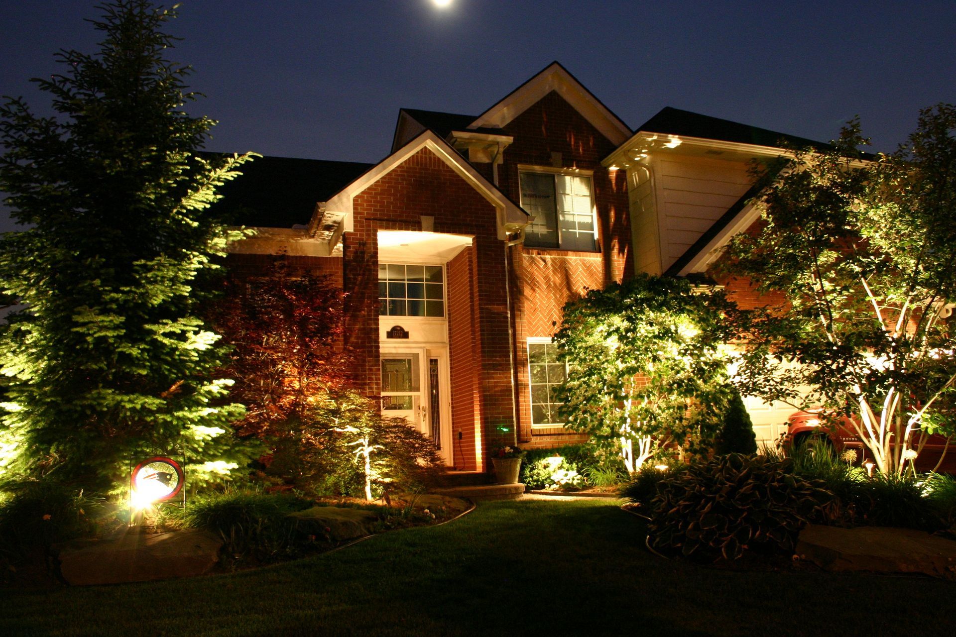 Night-lit house with landscaping, trees, and moon in the background.