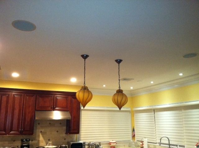 Kitchen ceiling with two pendant lights, recessed lights, and speakers. Cabinets, vent hood, and window blinds below.