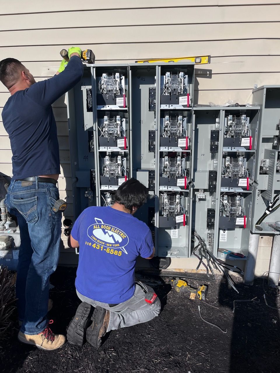 Two electricians installing electrical panels on a building exterior.