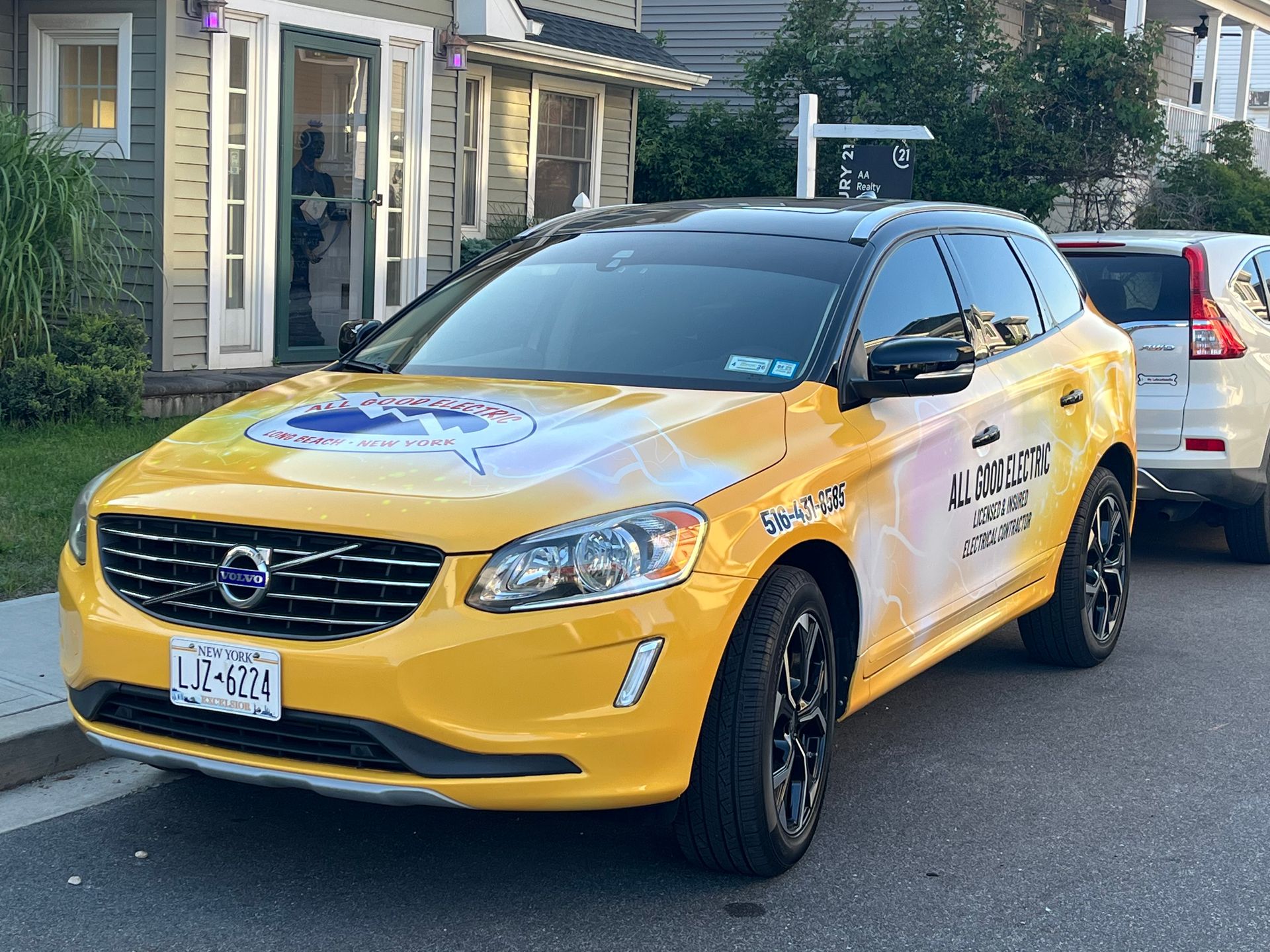 Yellow Volvo SUV with company logo parked on a street in front of a building.