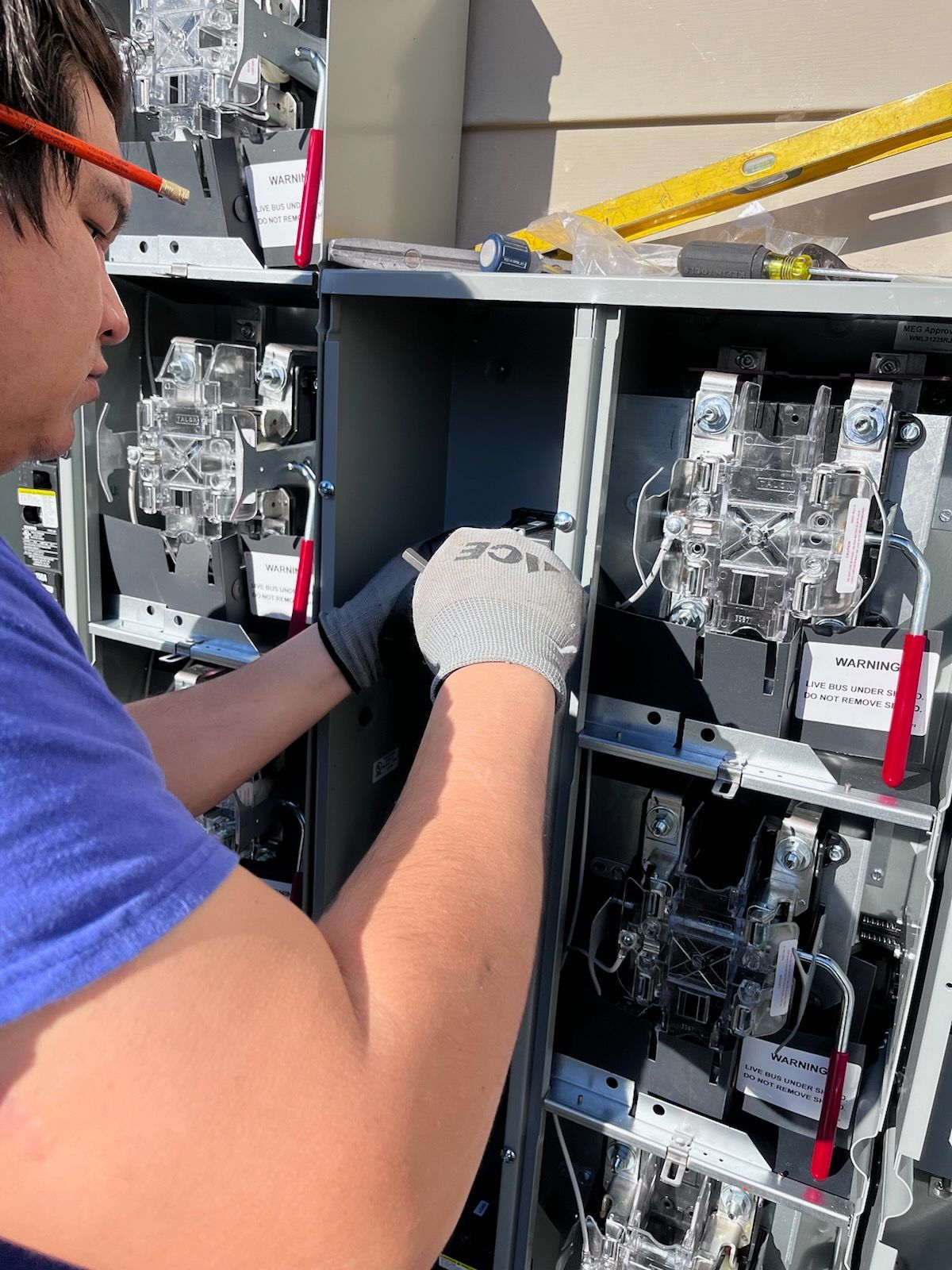 Man in work gloves wiring electrical panel. Outdoors, sunny.