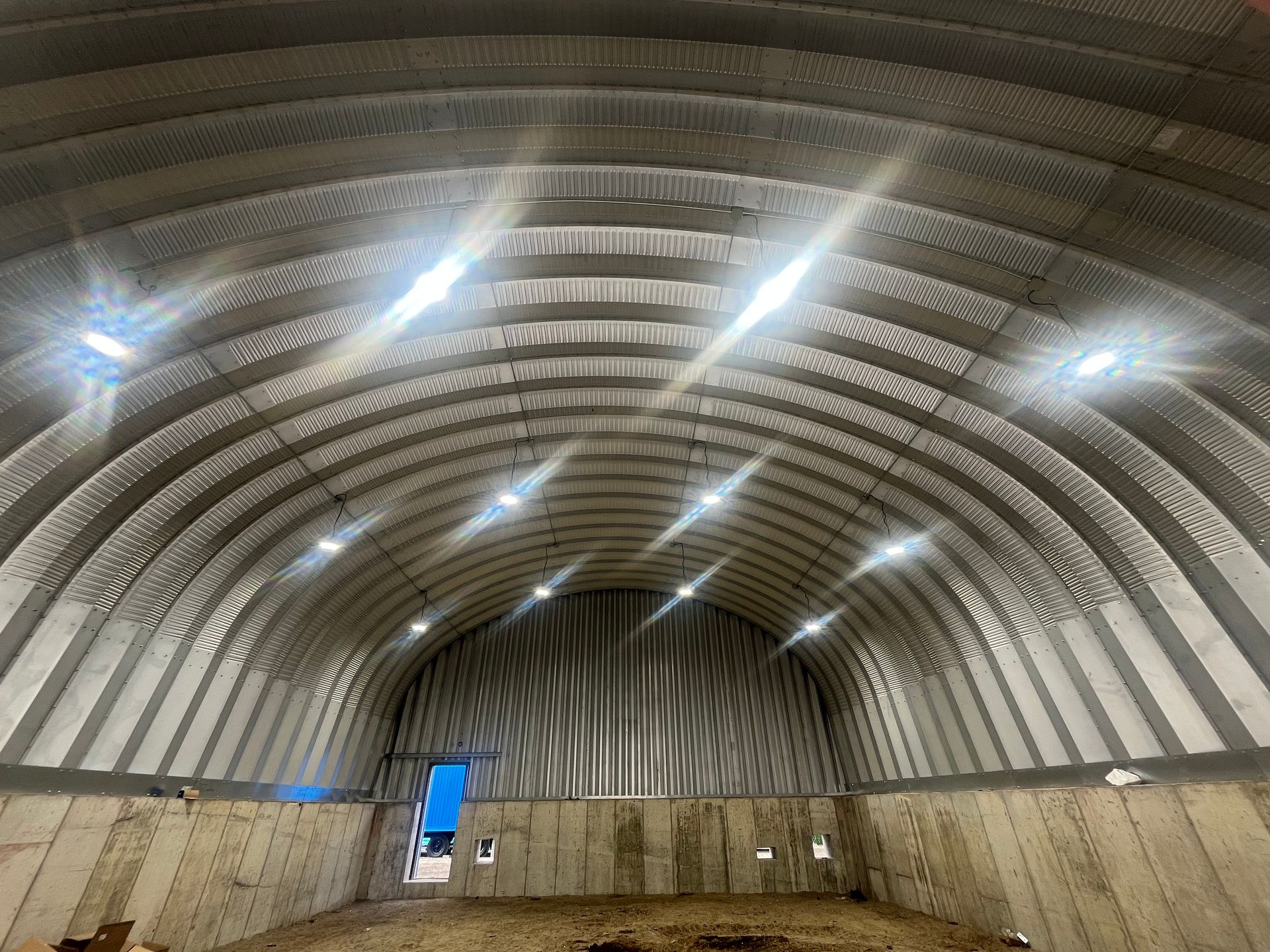Interior of a large, arched metal building with bright overhead lights and concrete walls.