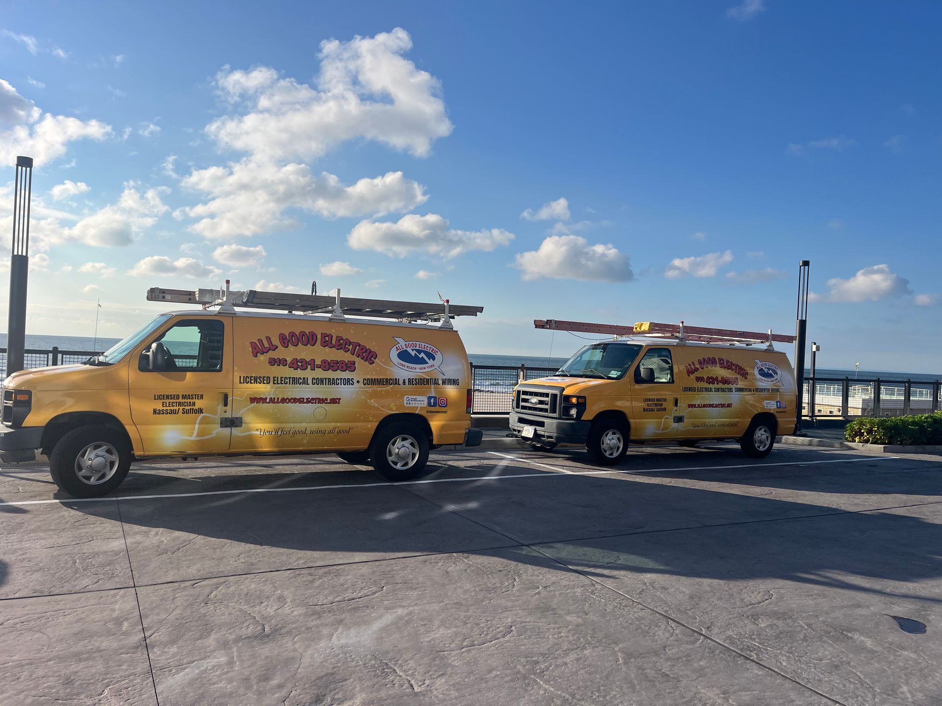 Two yellow service vans with ladders parked near water under a blue sky.