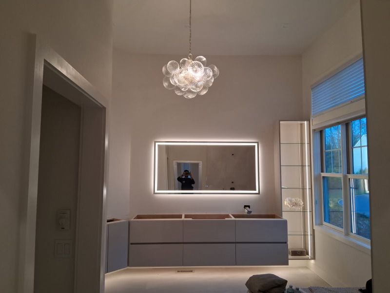 Modern bathroom with large mirror, vanity, and bubble chandelier; bright, neutral color palette.