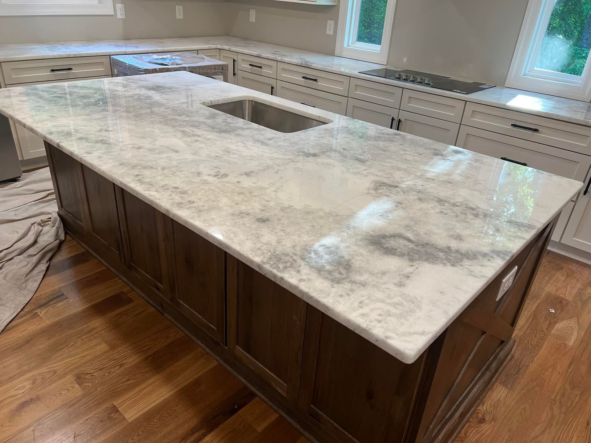 Kitchen island with marble countertop and dark wooden cabinets, sink, and hardwood floor.
