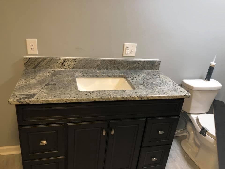 Dark brown bathroom vanity with granite countertop, sink, and toilet against a gray wall.
