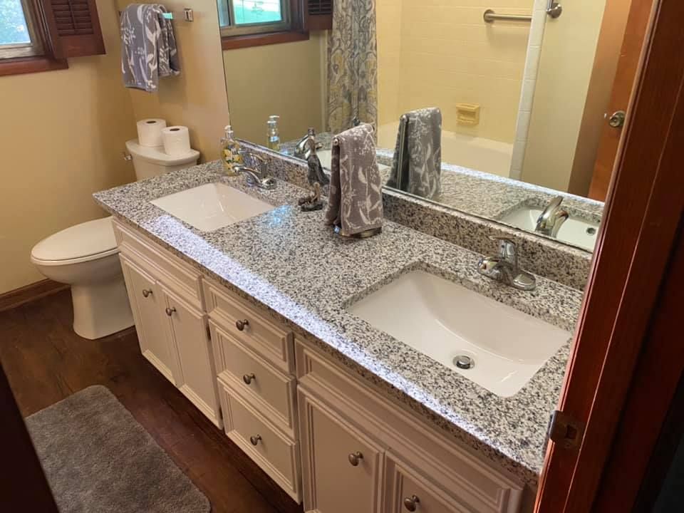 Bathroom with double sinks, granite countertop, white cabinets, and beige walls.