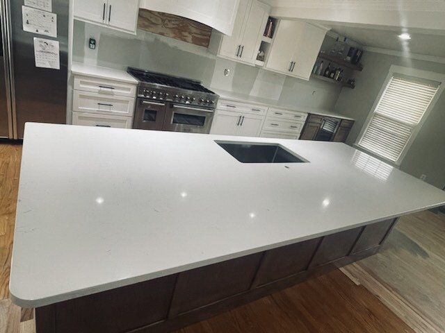 Modern kitchen with white countertops and dark wood island. Sink in island, stainless steel range.