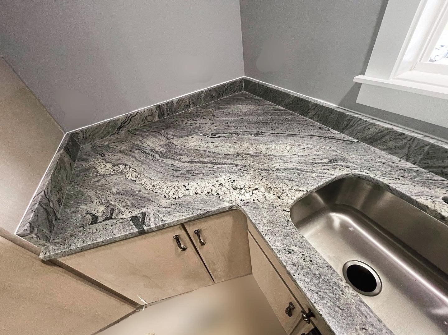 Granite countertop with a stainless steel sink over light-colored cabinets in a kitchen.