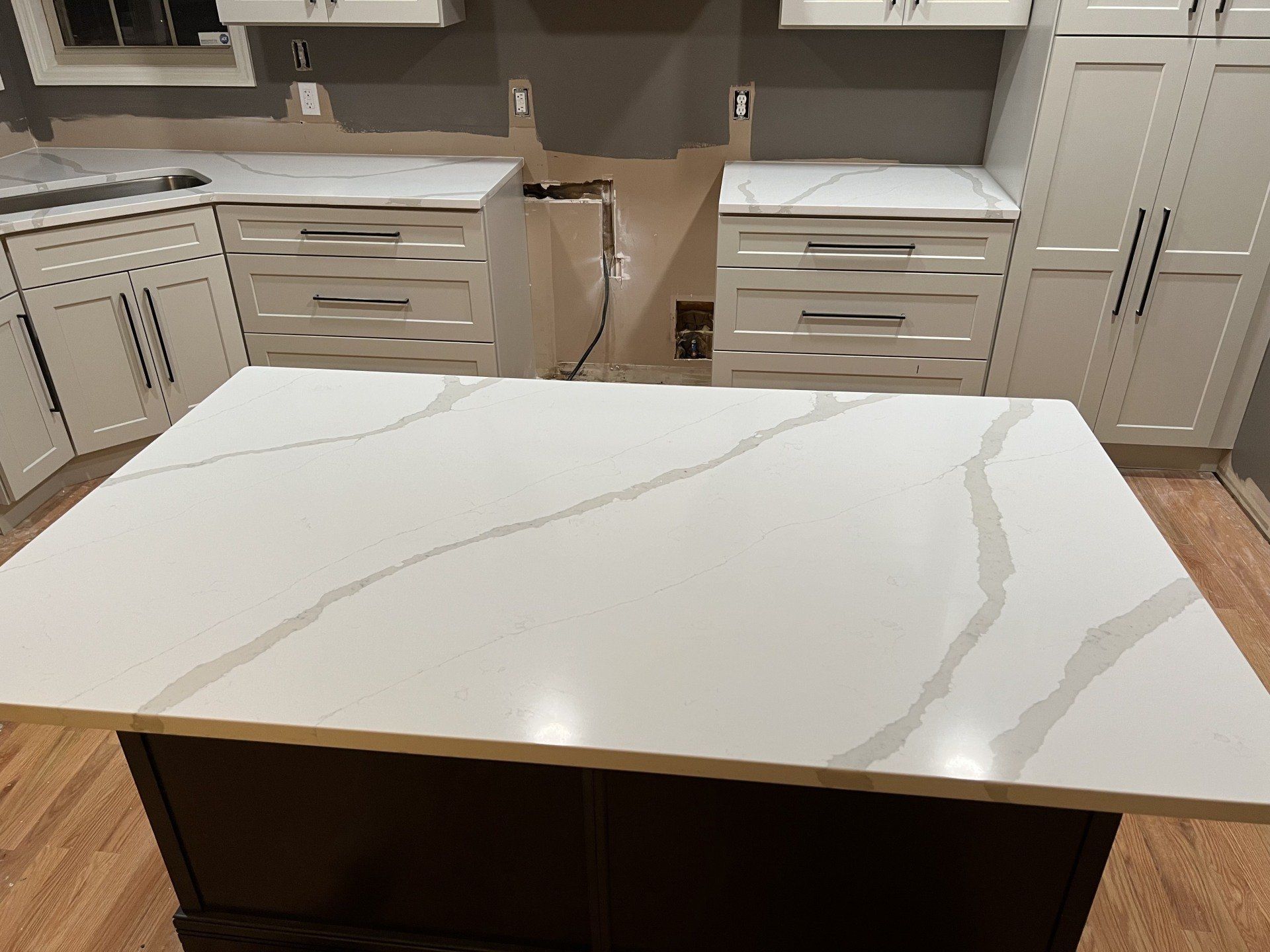 Kitchen with white quartz countertops and dark brown island, white cabinets.