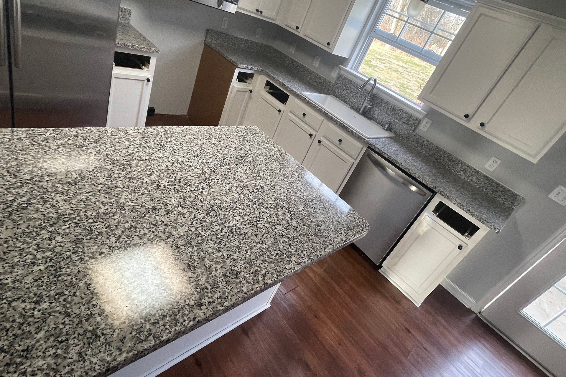 Kitchen with granite countertops, white cabinets, stainless steel appliances, and hardwood floors.